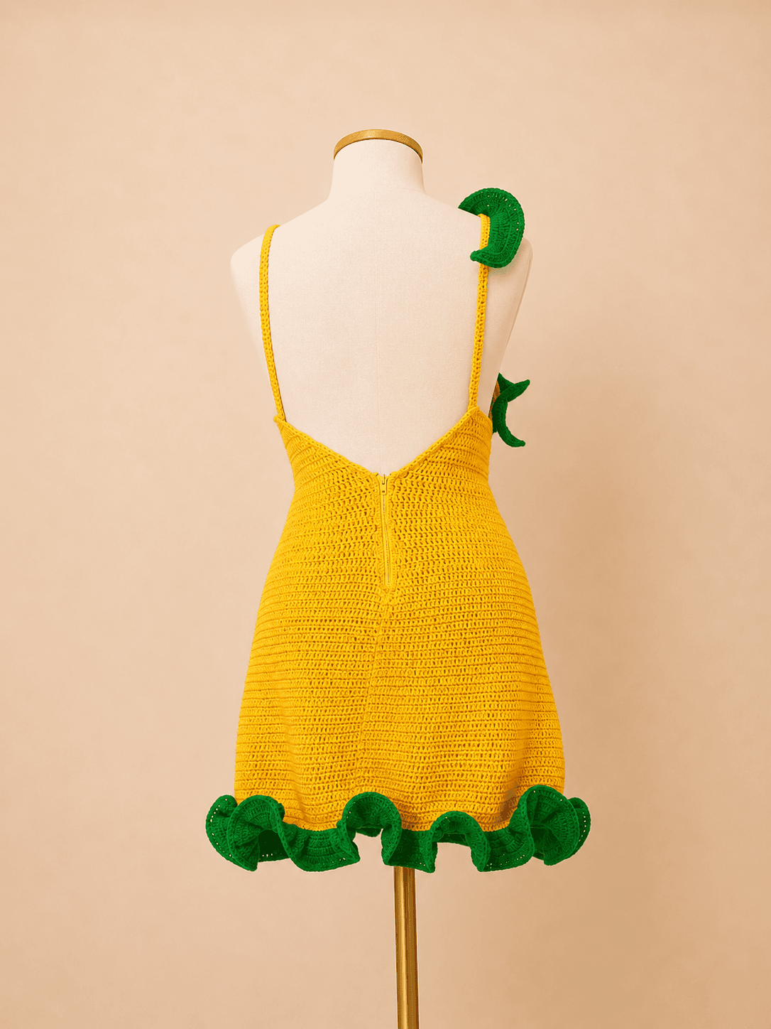 Vestido tropical em crochê amarelo com babados verdes, feito à mão em fio de algodão, exibido em manequim off white com fundo bege suave