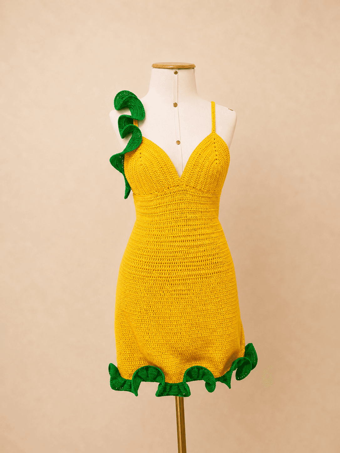 Vestido tropical em crochê amarelo com babados verdes, feito à mão em fio de algodão, exibido em manequim off white com fundo bege suave